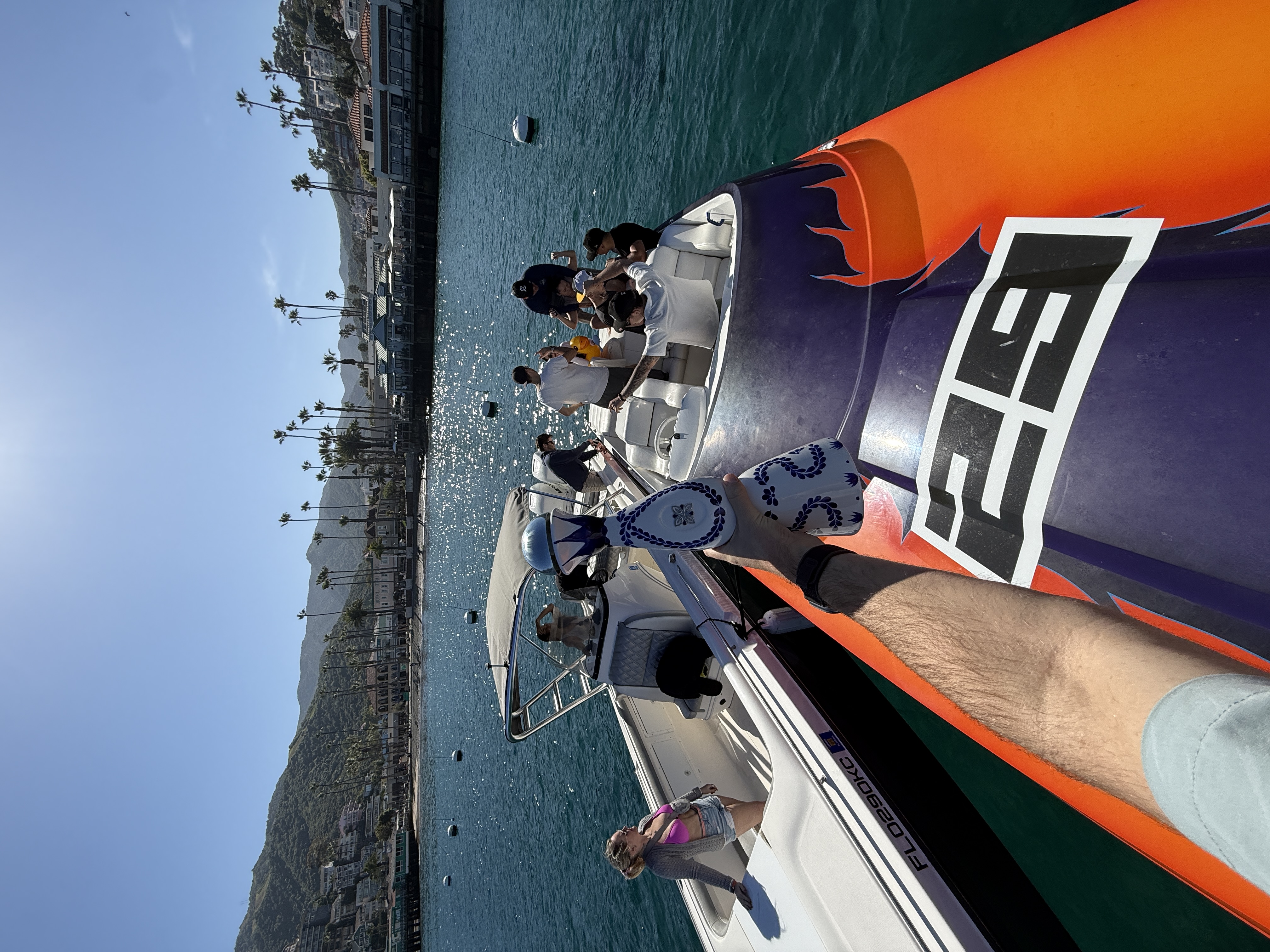 Man in red trunks on boat stern holding Clase Azul tequila, Avalon waterfront behind