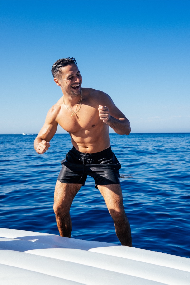 Shirtless man laughing on the bow with blue ocean behind him
