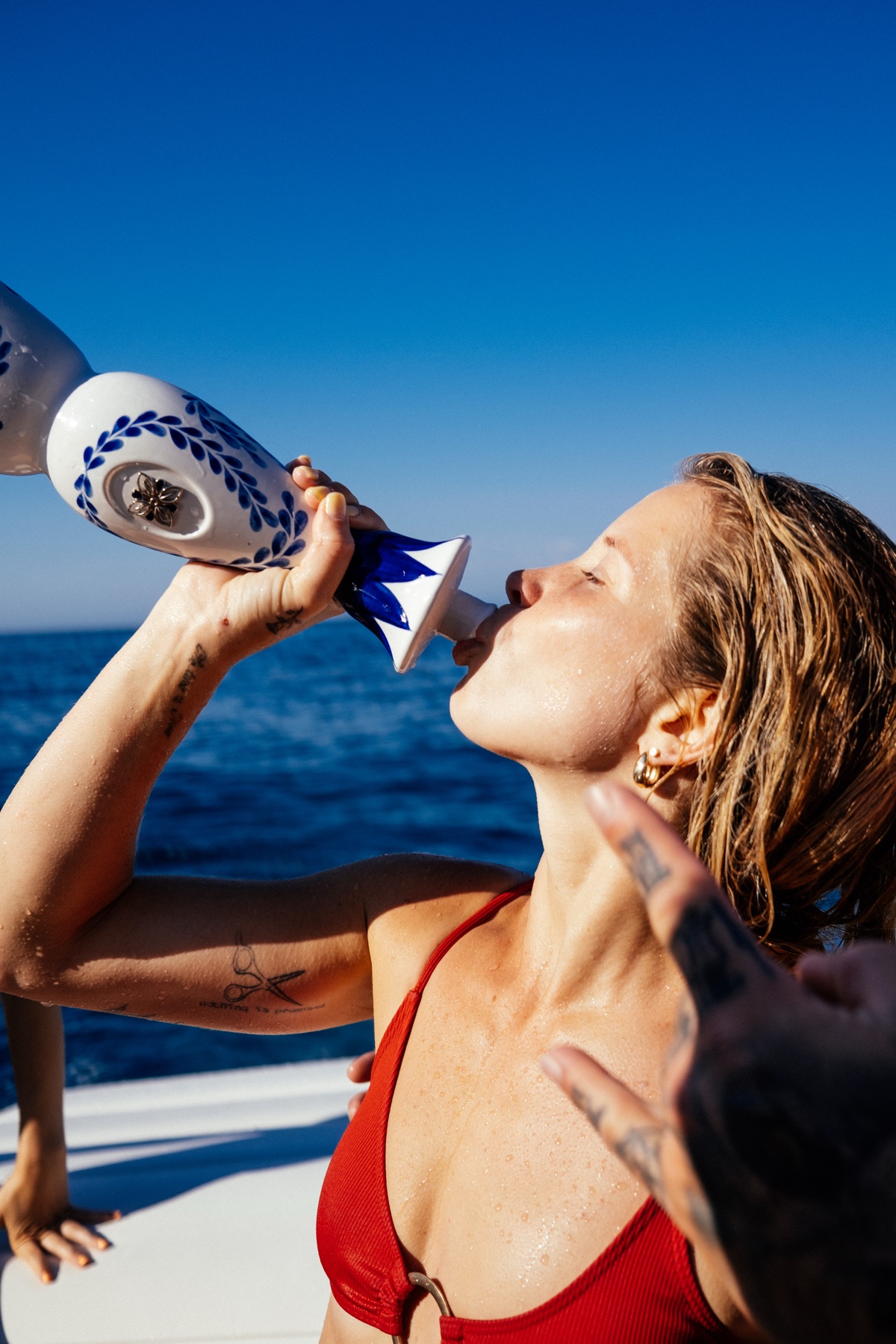 Woman in red bikini drinking Clase Azul tequila straight from the bottle on a boat