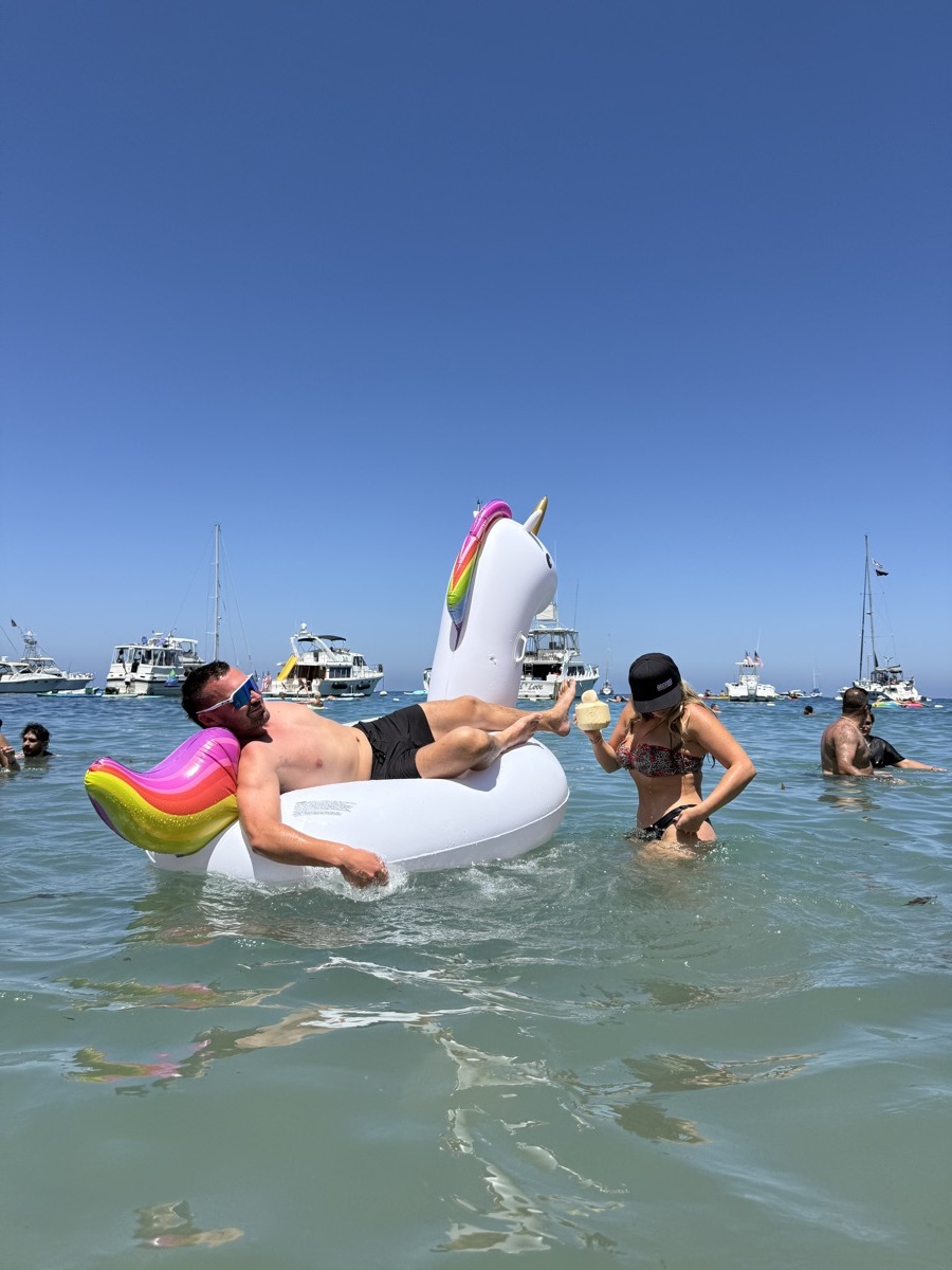 Guy lounging on a unicorn float with boats anchored behind