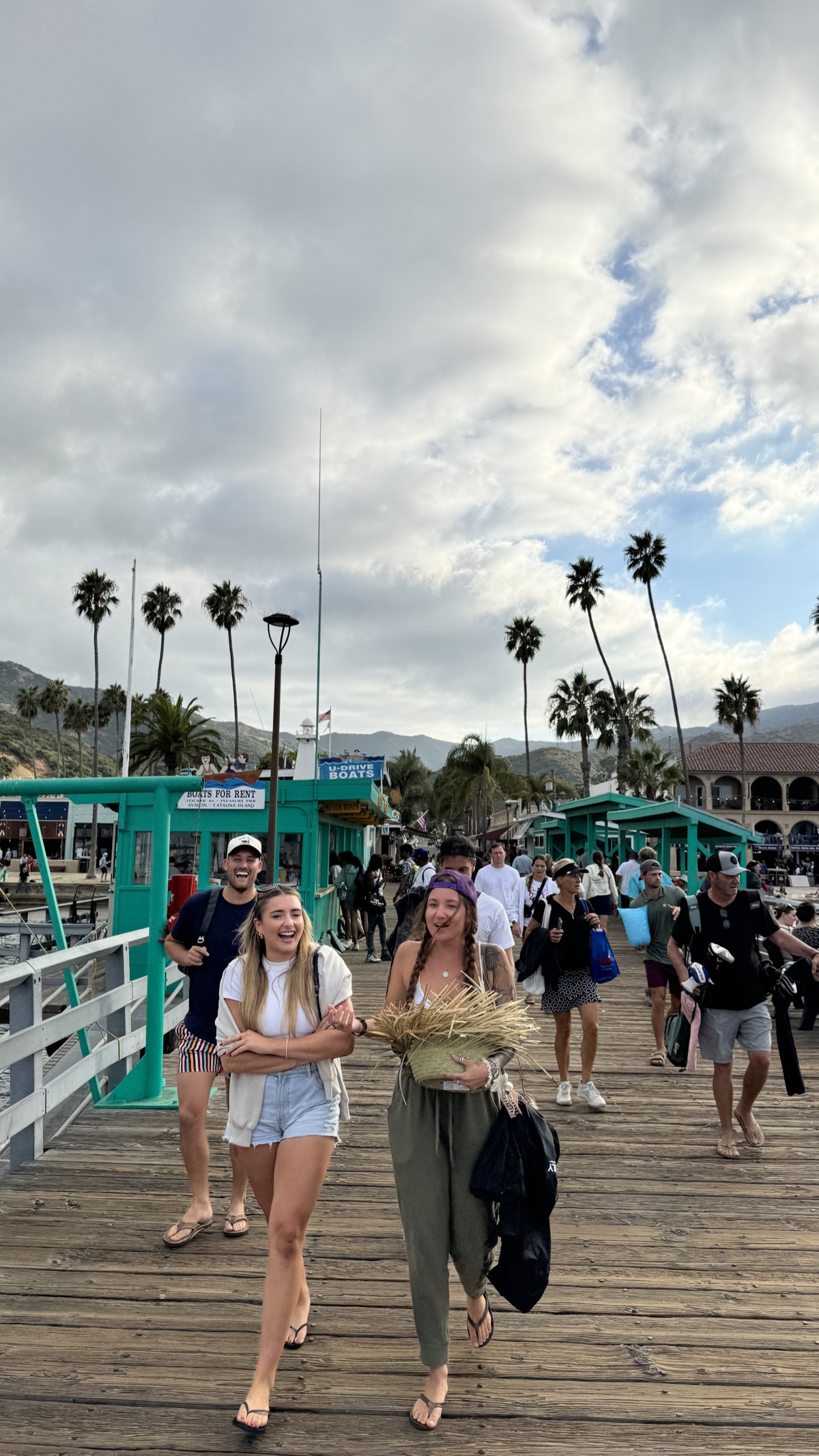 Two people walking down the Avalon pier with palm trees overhead